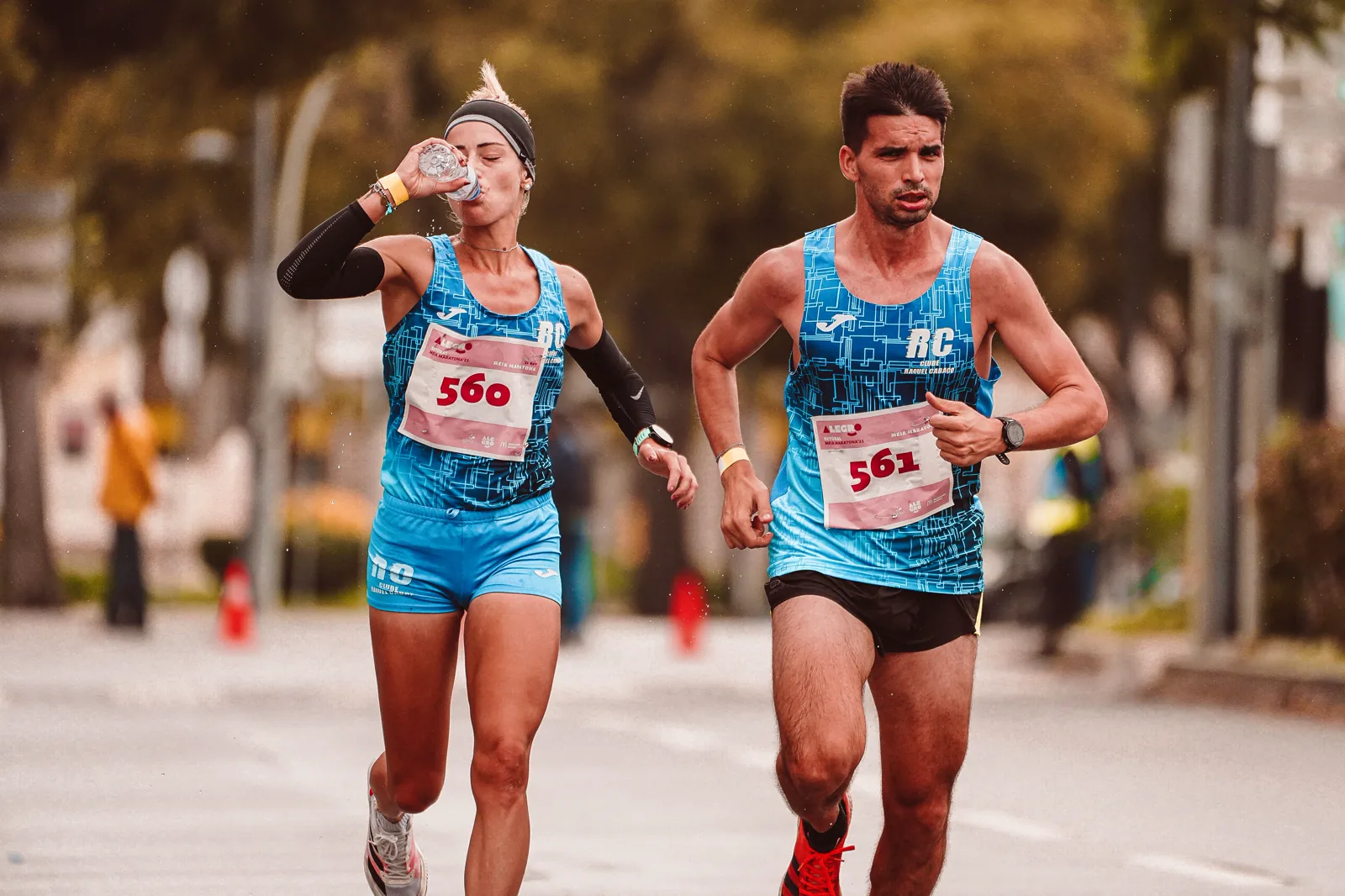 Dois atletas correndo uma meia maratona enquanto uma corredora bebe água