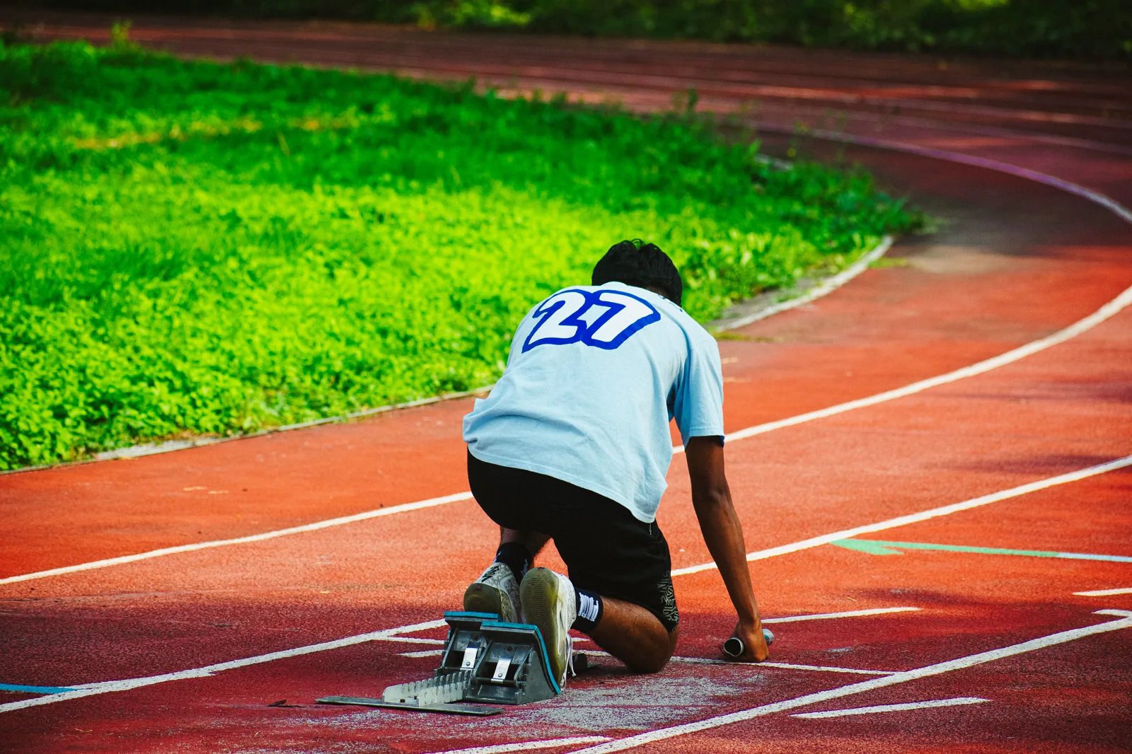 Atleta posicionado no bloco de partida de uma pista de atletismo